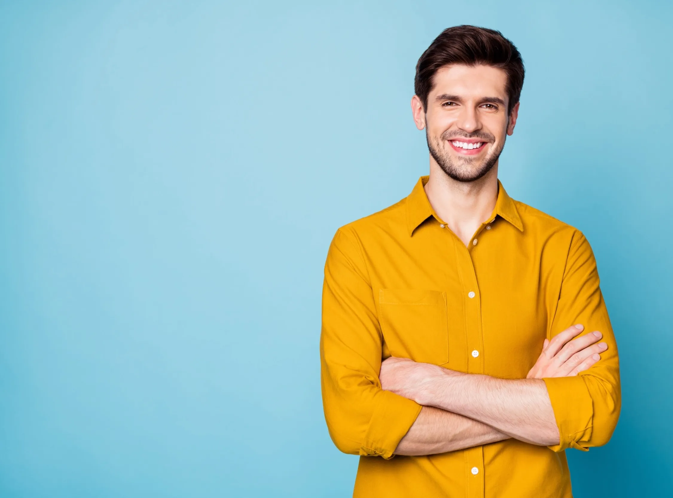 Smiling person in bright yellow shirt standing with crossed arms