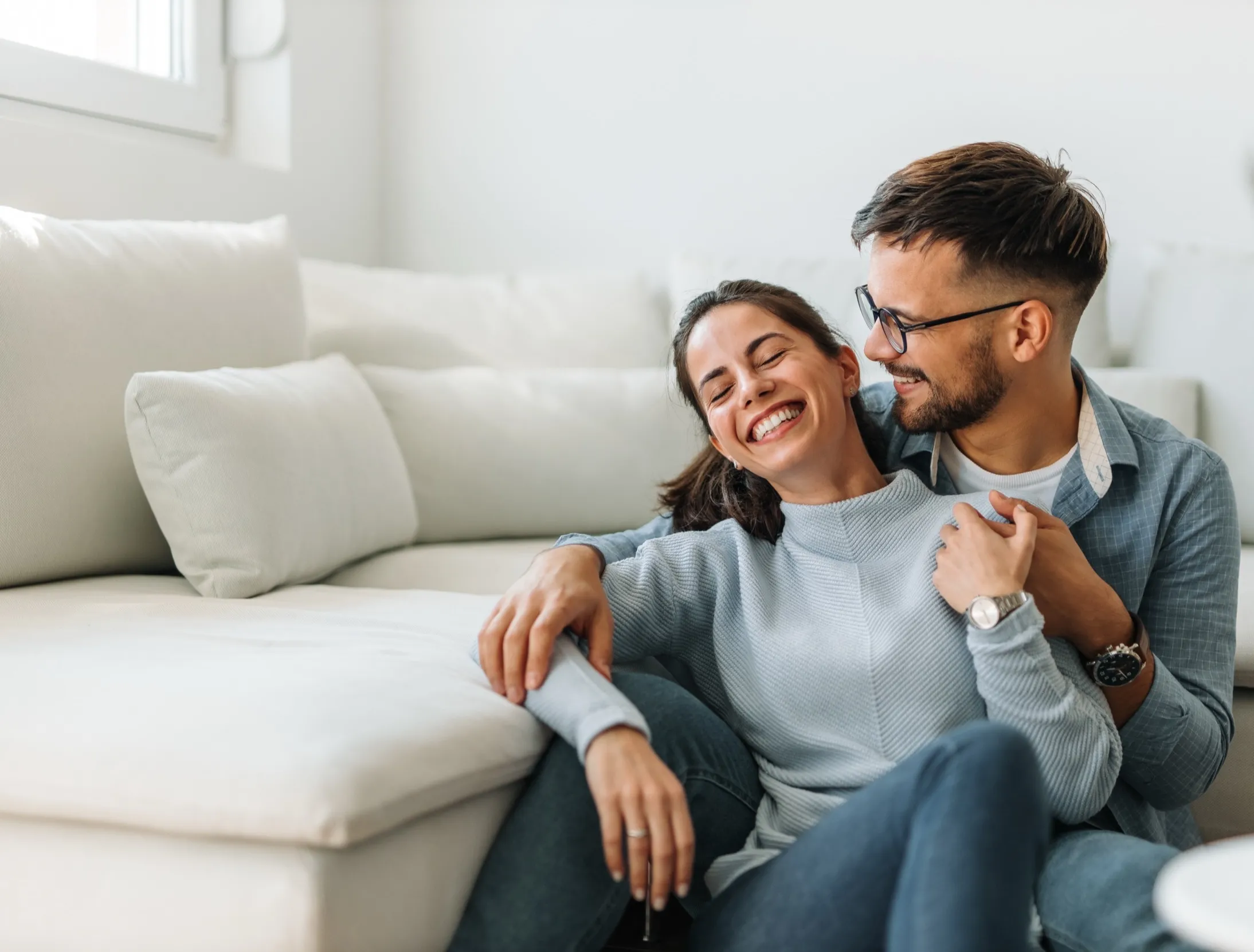 Couple laughing together on couch, embracing in comfortable living room