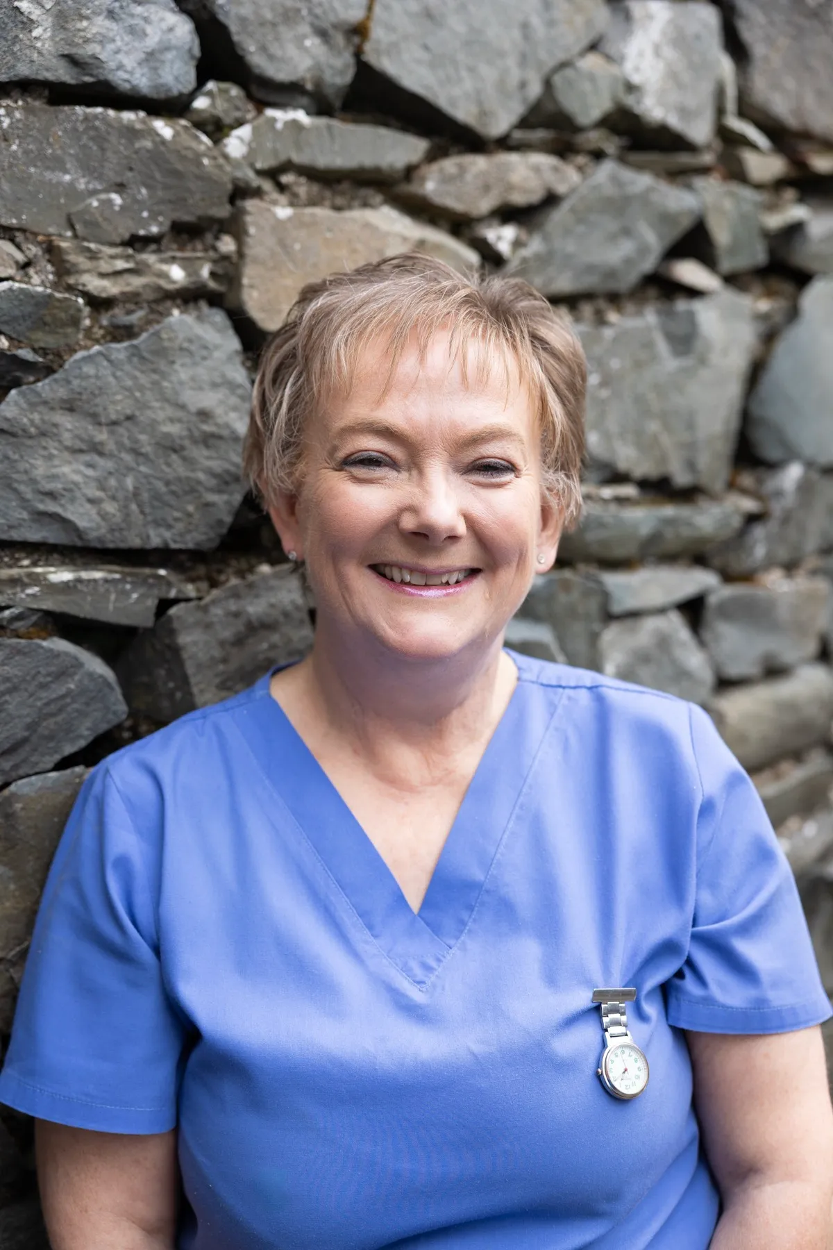 Smiling healthcare worker in blue scrubs against stone wall background