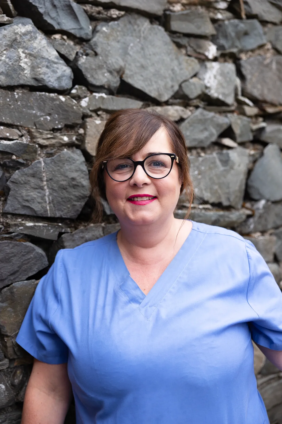 Smiling healthcare worker in blue scrubs standing against stone wall