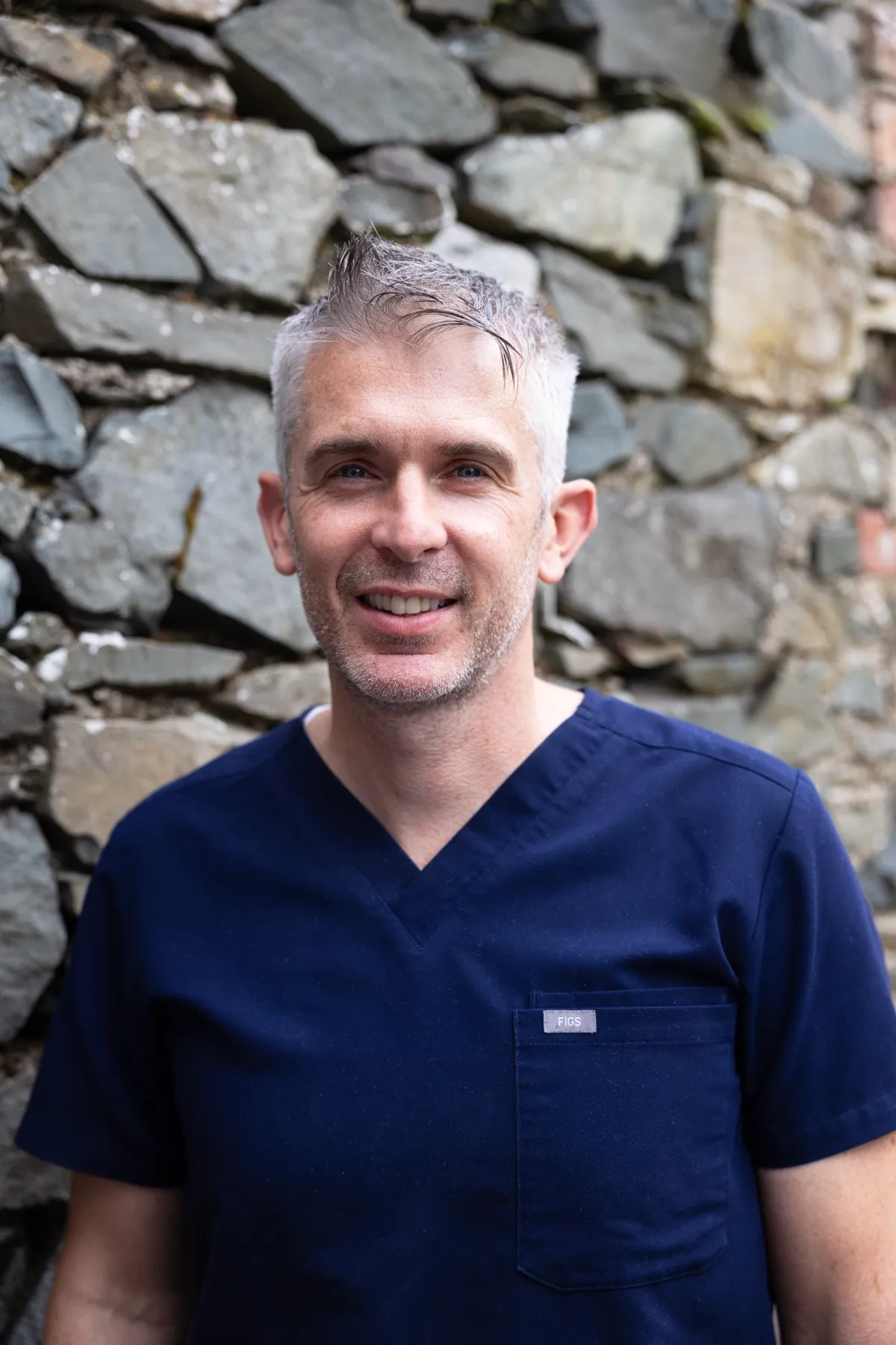 Smiling healthcare professional in blue scrubs against stone wall background