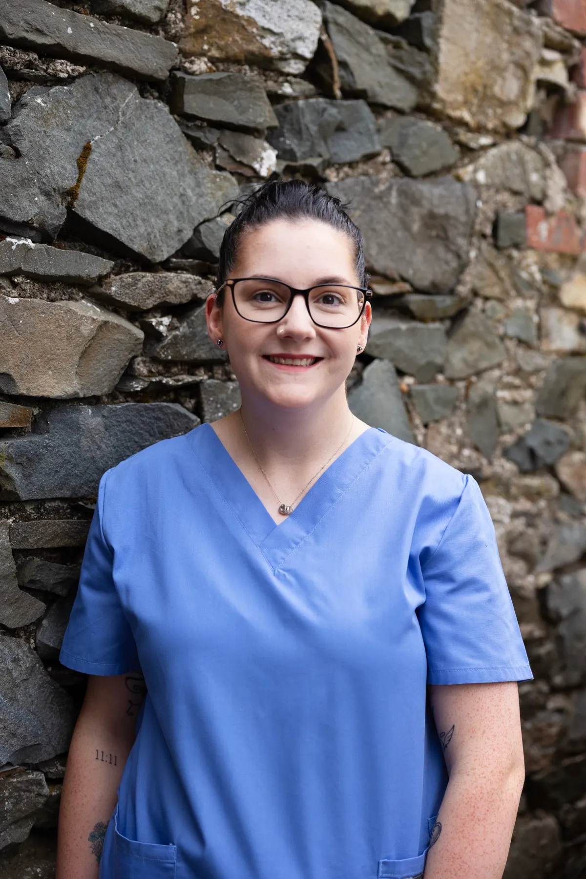 Smiling healthcare professional in blue scrubs against stone wall background