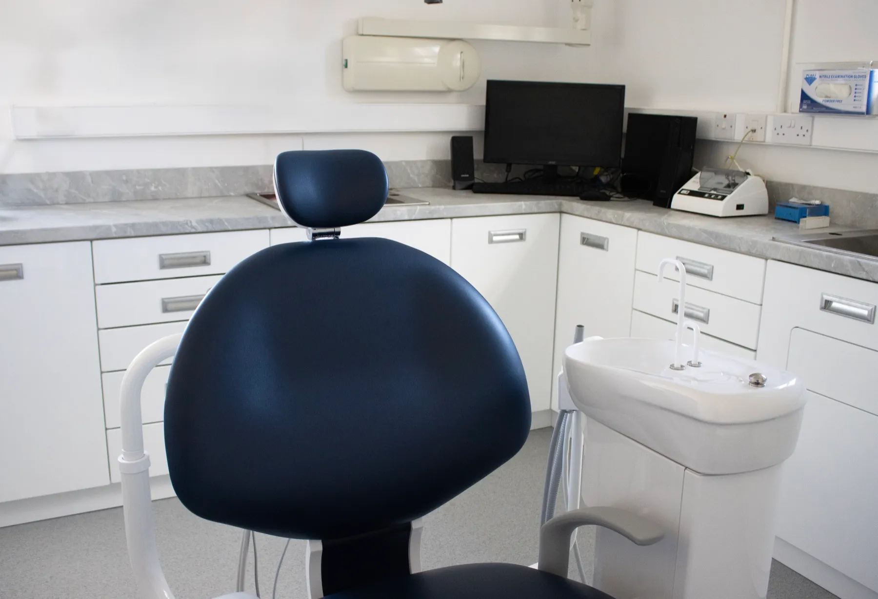 Dental office interior with blue chair, sink, and computer workstation