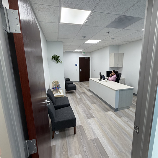 Clinic reception area with a staff member at the front desk, comfortable waiting chairs, and light wood flooring.