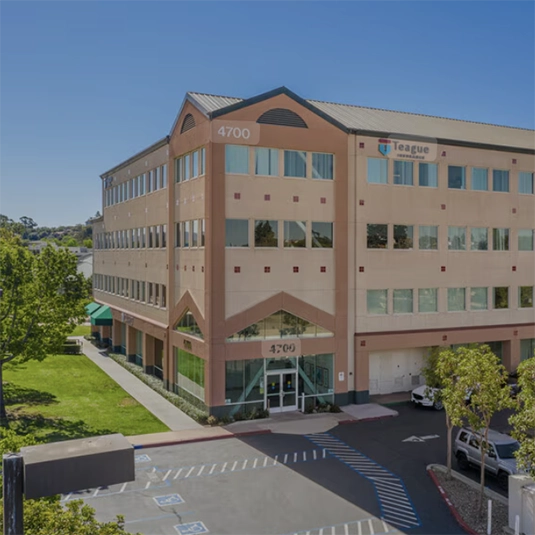 Exterior of the 4700 Spring Street office building, a four-story tan commercial building with surrounding trees and a parking lot.