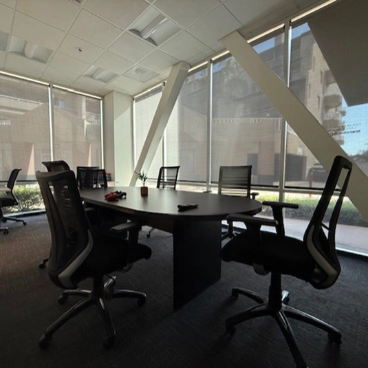 Conference room with an oval table, ergonomic chairs, and floor-to-ceiling windows overlooking the surrounding property.