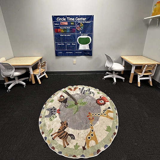 Circle Time Center with animal-themed rug Circle Time Center with student desks, an animal-themed rug, and visual learning charts for group activities.