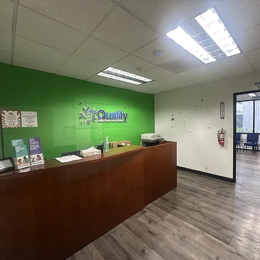 Front reception area with a wood welcome desk, a green accent wall with clinic signage, brochures, and a fire extinguisher by the entrance.