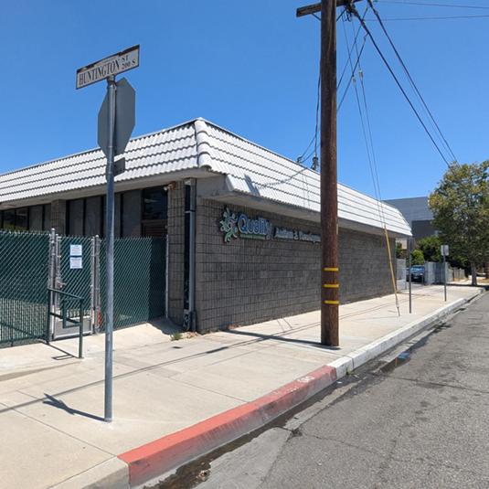Street view of the San Fernando clinic, a single-story building on a corner lot with a white tiled roof, brick walls, and a fenced side entrance.