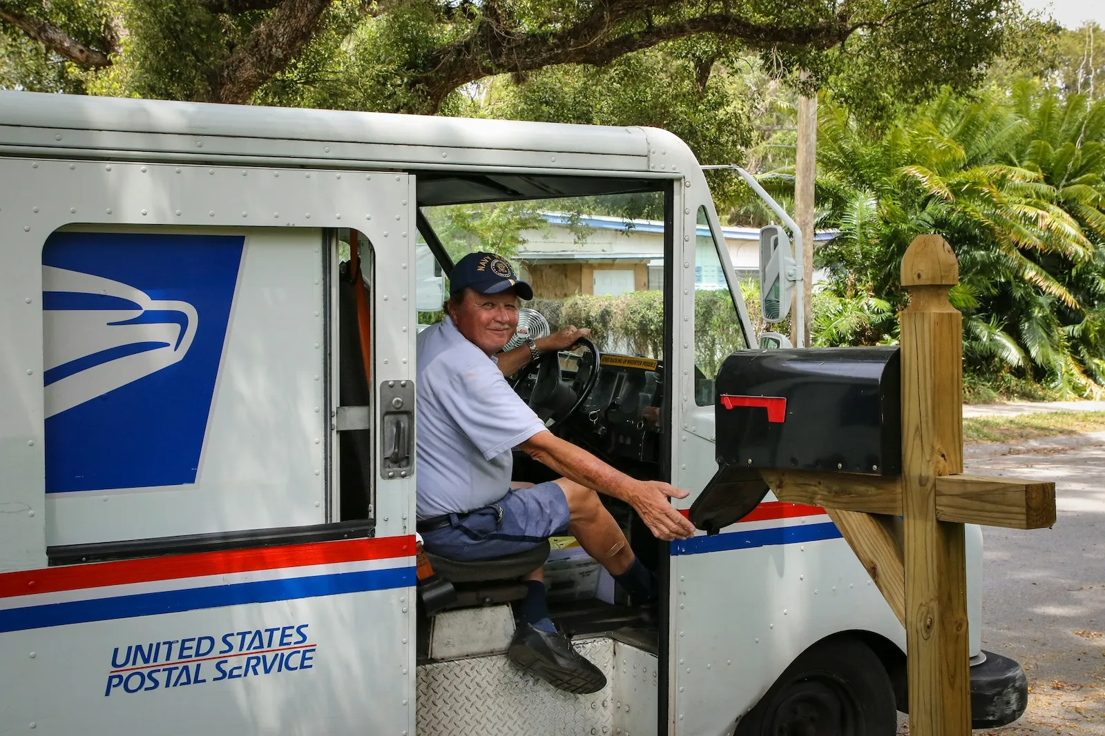 USPS mail carrier delivering mail to mailbox, representing mail handling and forwarding services