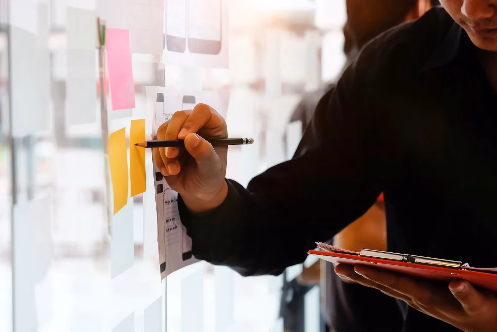 Business professional organizing workflow and risk planning on glass board with sticky notes