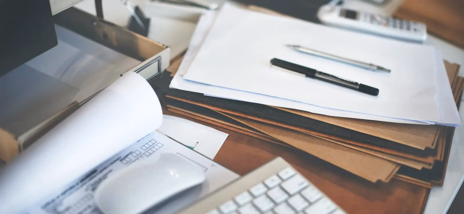 Cluttered office desk with piles of unsorted business documents and paperwork