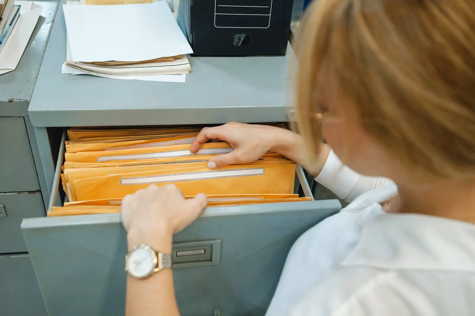 Office worker manually searching through paper files in a metal filing cabinet, illustrating outdated business mail management