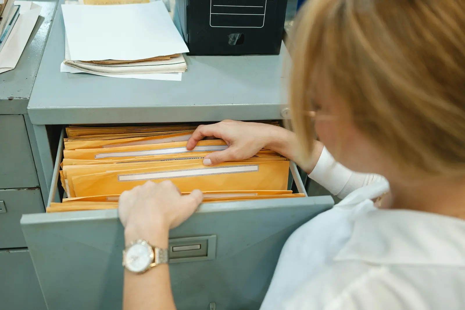 Office worker manually searching through paper files in a metal filing cabinet, illustrating outdated business mail management