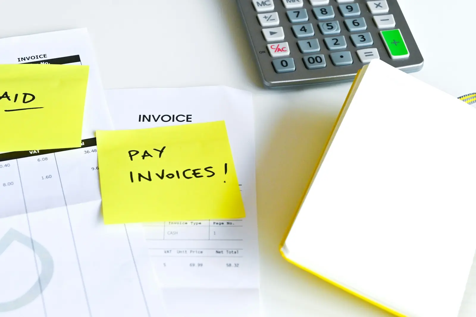 Invoice paperwork with a 'Pay Invoices' sticky note reminder next to a calculator, representing manual accounts payable workflows small businesses automate by connecting mail to QuickBooks and Xero