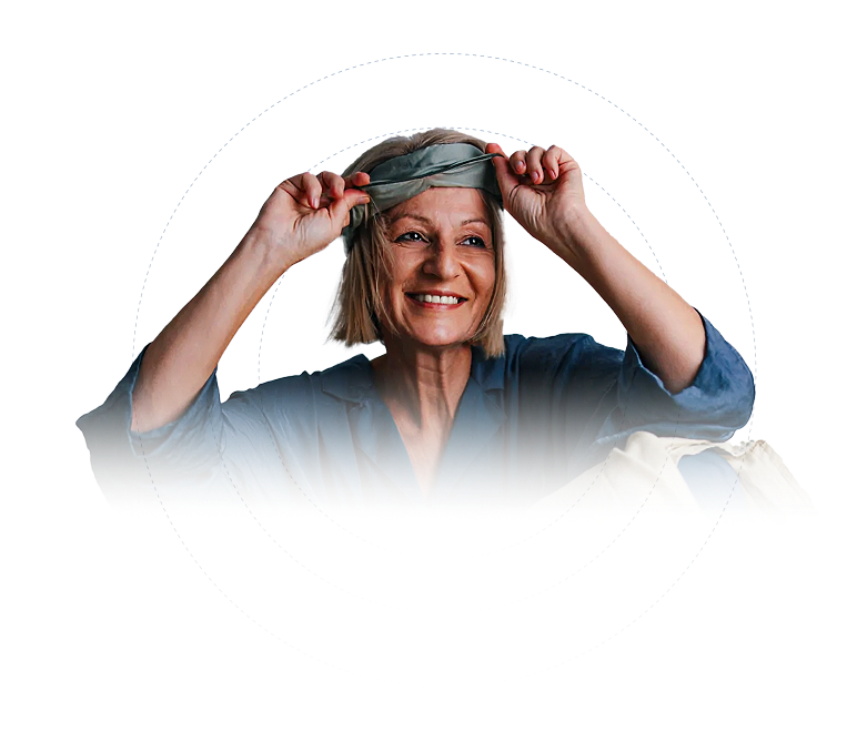 Smiling middle-aged woman putting on a gray sleep mask while wearing blue pajamas.
