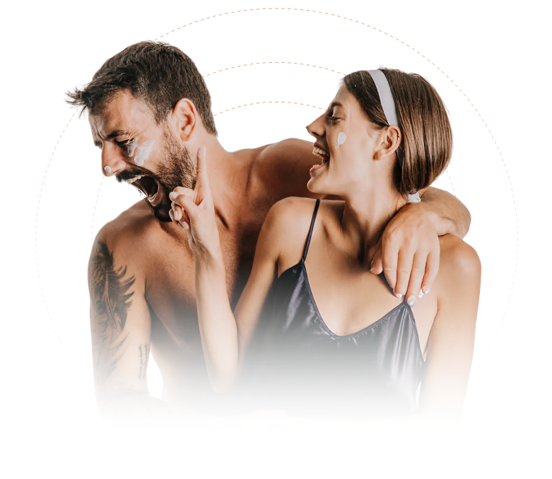 Smiling man and woman with skincare cream on their faces, sharing a playful moment together.