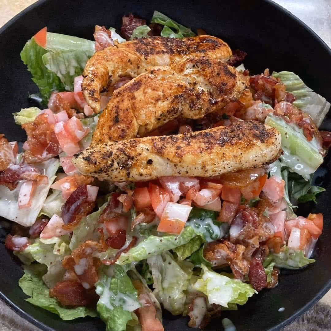 A bowl of salad with chicken and bacon.