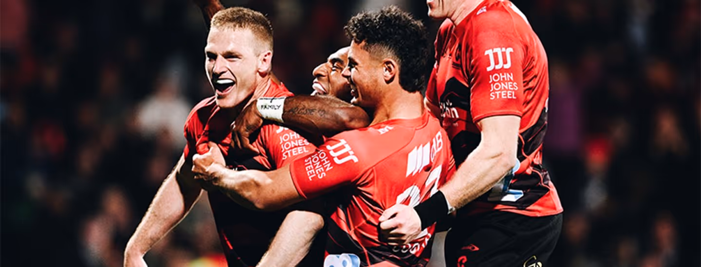Four rugby players in red jerseys celebrating a moment on the field.