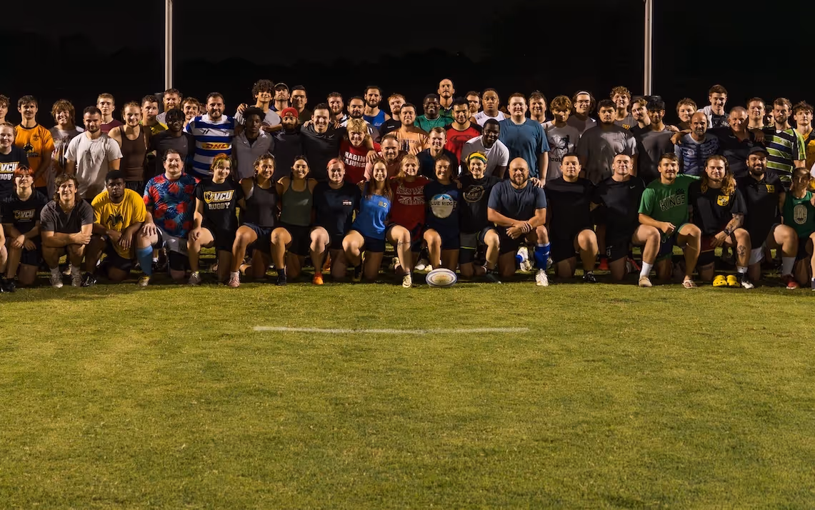 Large group of diverse rugby players posing together on a grassy field at night.