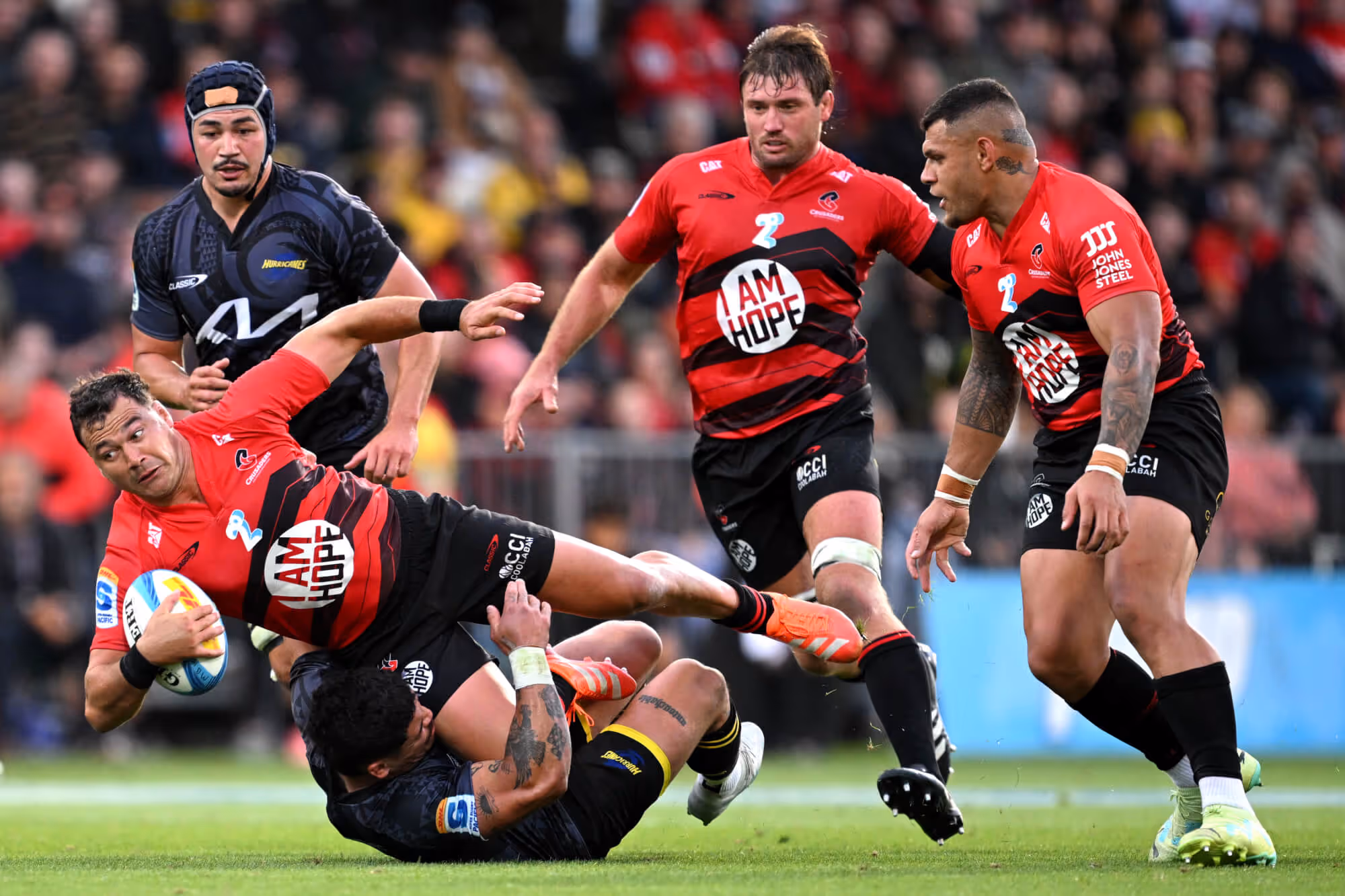 Rugby players in red and black jerseys tackling an opponent wearing black during a match.
