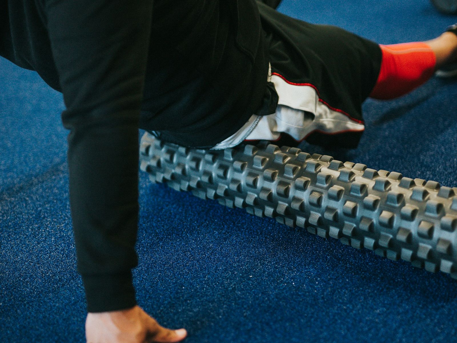 Person using a foam roller on the side of the hip and thigh on a gym floor.
