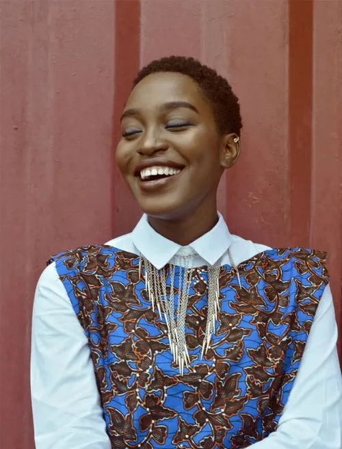 A woman smiling while wearing a blue and white shirt, exuding a cheerful and positive demeanor.