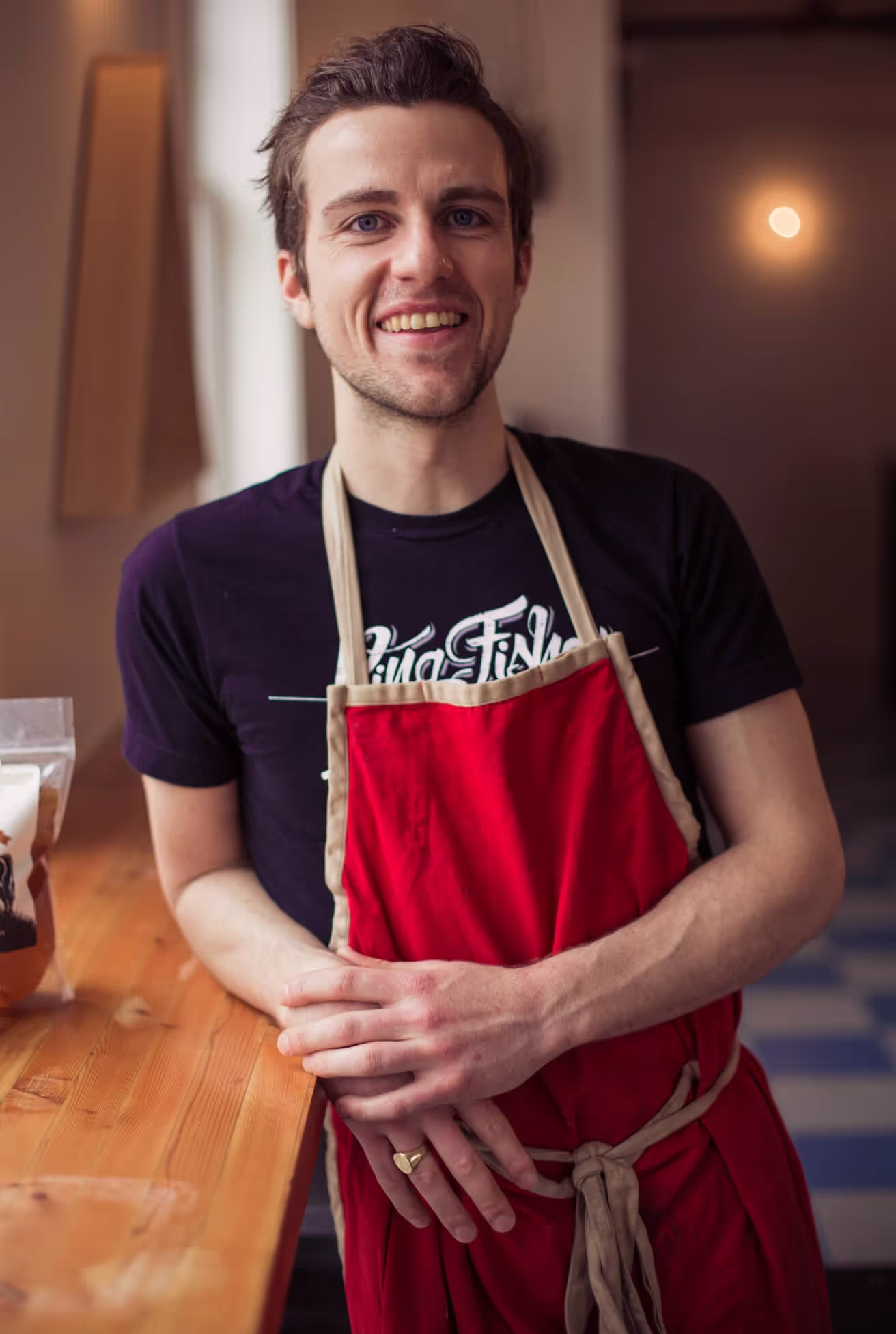 A man wearing an apron stands confidently in front of a table, ready to prepare a meal or engage in culinary activities.