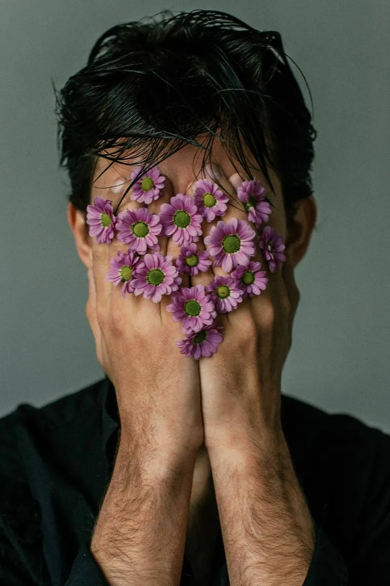 A man obscuring his face with a vibrant arrangement of flowers, creating a striking and artistic visual effect.