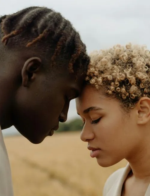 A young couple stands in a field, eyes closed, enjoying a serene moment together amidst nature.