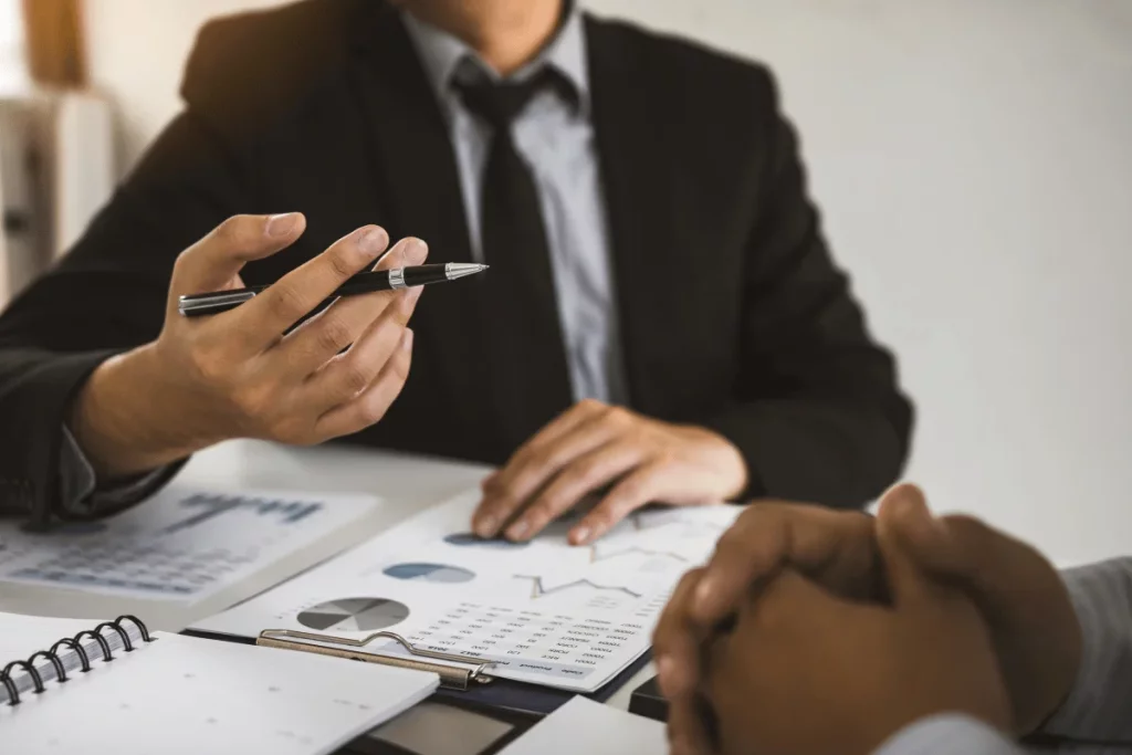 Business professional in a suit discussing financial charts and data during a meeting with a colleague.