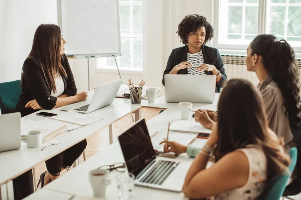 A group of professionals in a meeting with laptops on a table.