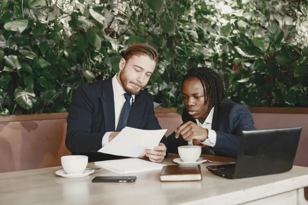 Colleagues discussing paperwork while seated at a table in a cafe with greenery.