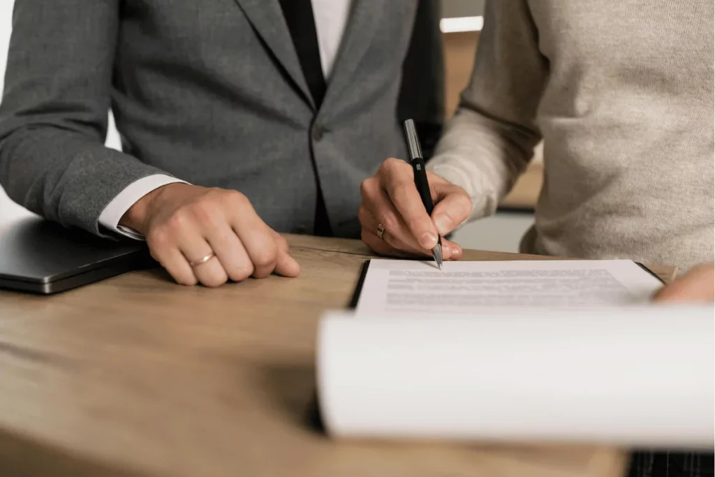 Hands of two people writing on a contract at a desk.
