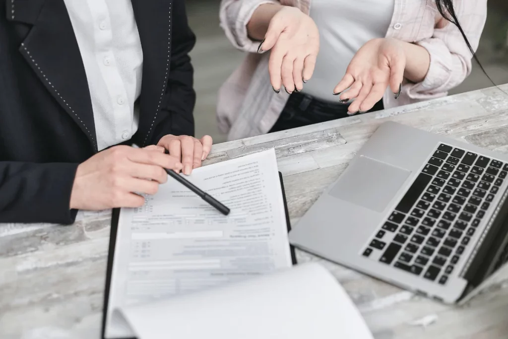 Two people reviewing forms, with a laptop and pointing gestures.