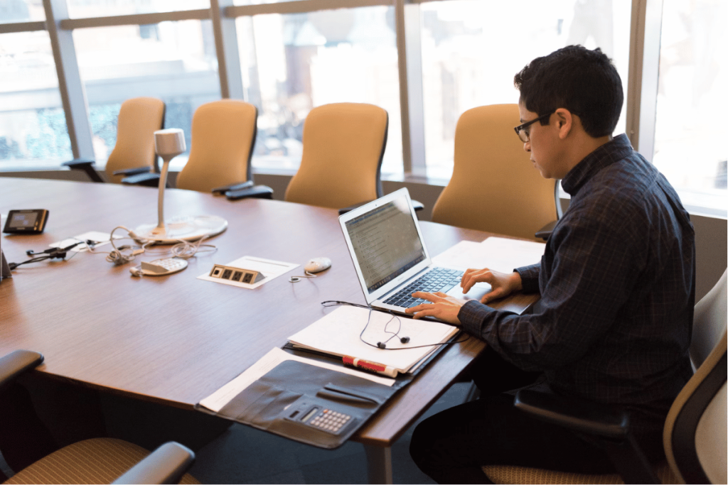 A person sitting at a conference table using a laptop.