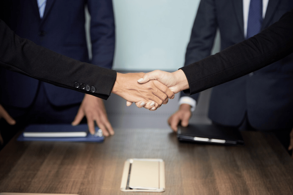 Two individuals shaking hands over a table.