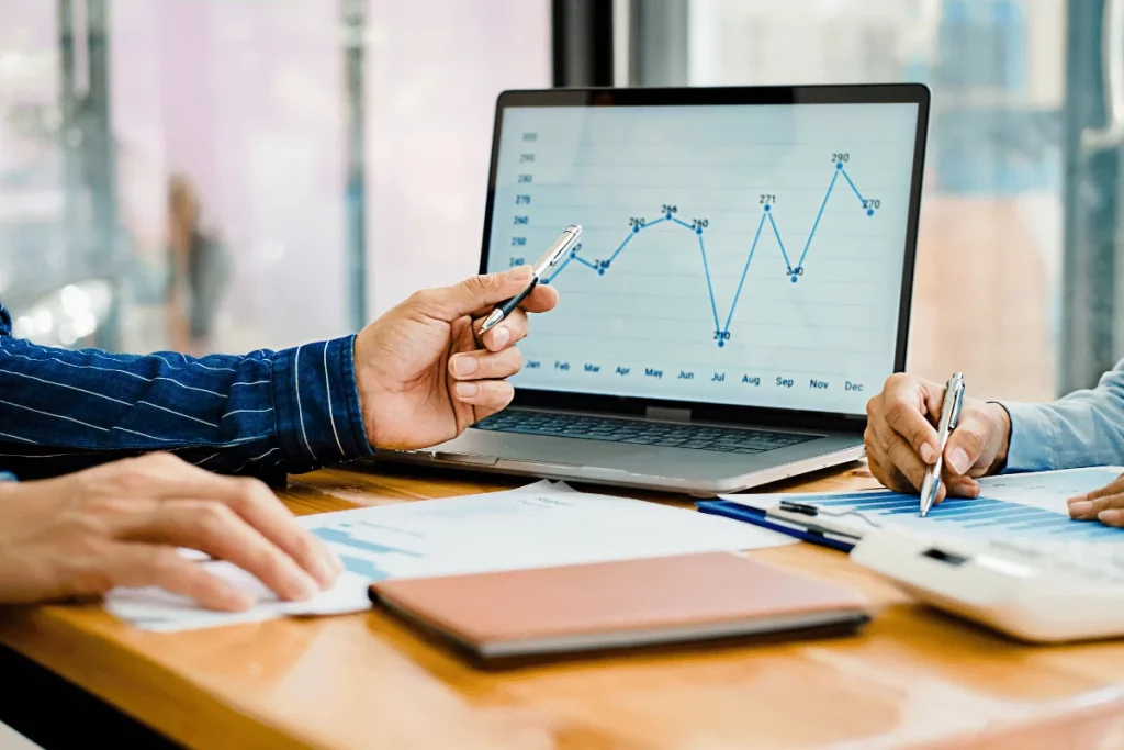 Business professionals discussing financial data shown on a laptop screen.