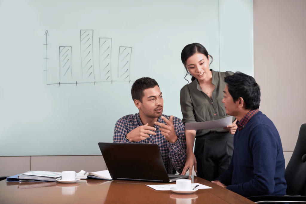 Three people sitting around a table with a laptop.