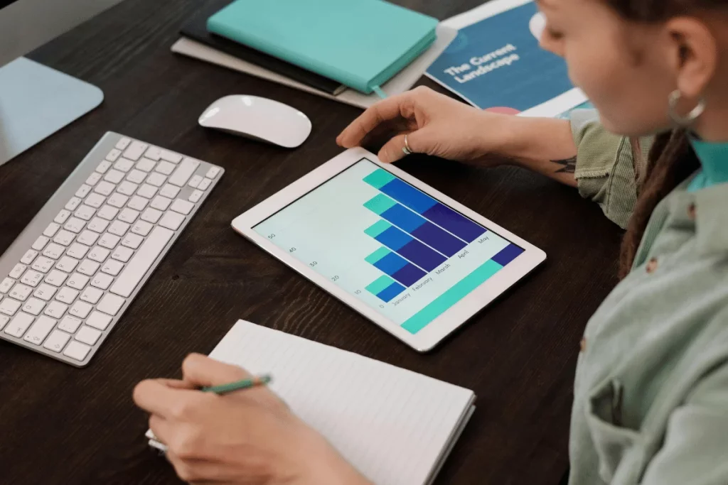 Person analyzing colorful bar graph on a tablet with notepad in hand.