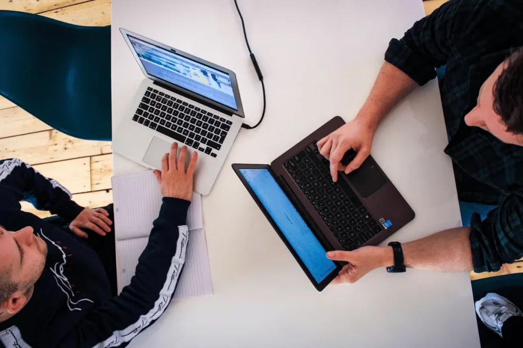 Overhead view of two people working on laptops at a white table.
