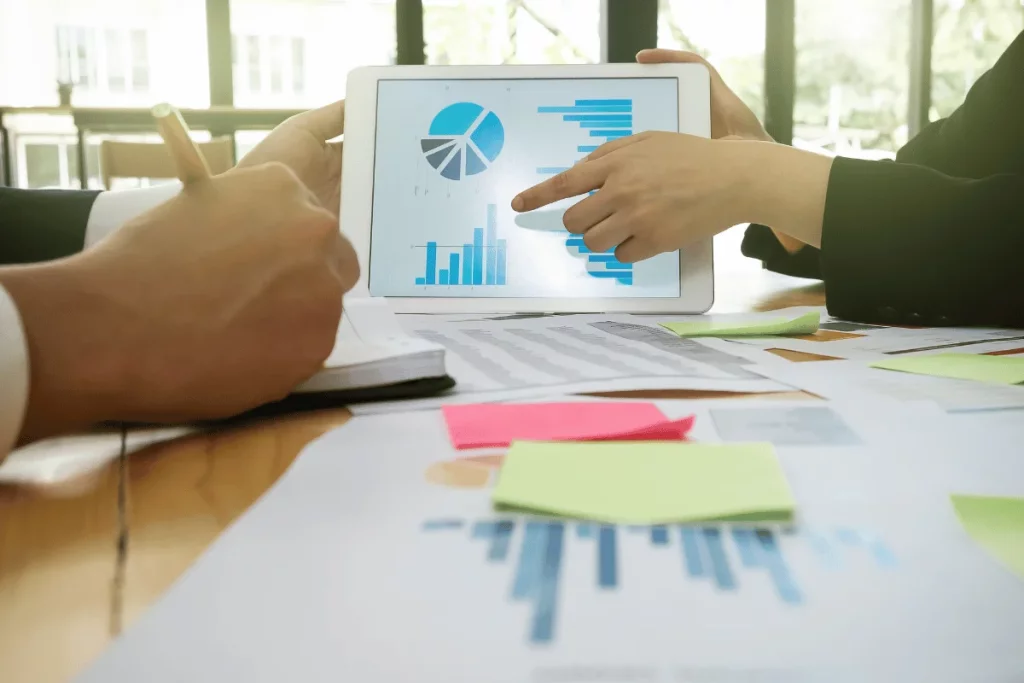 Business meeting with tablet displaying financial charts and hands pointing at data.