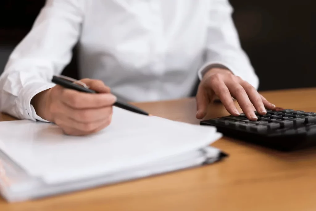 Person in white shirt using calculator to work through accounting paperwork.