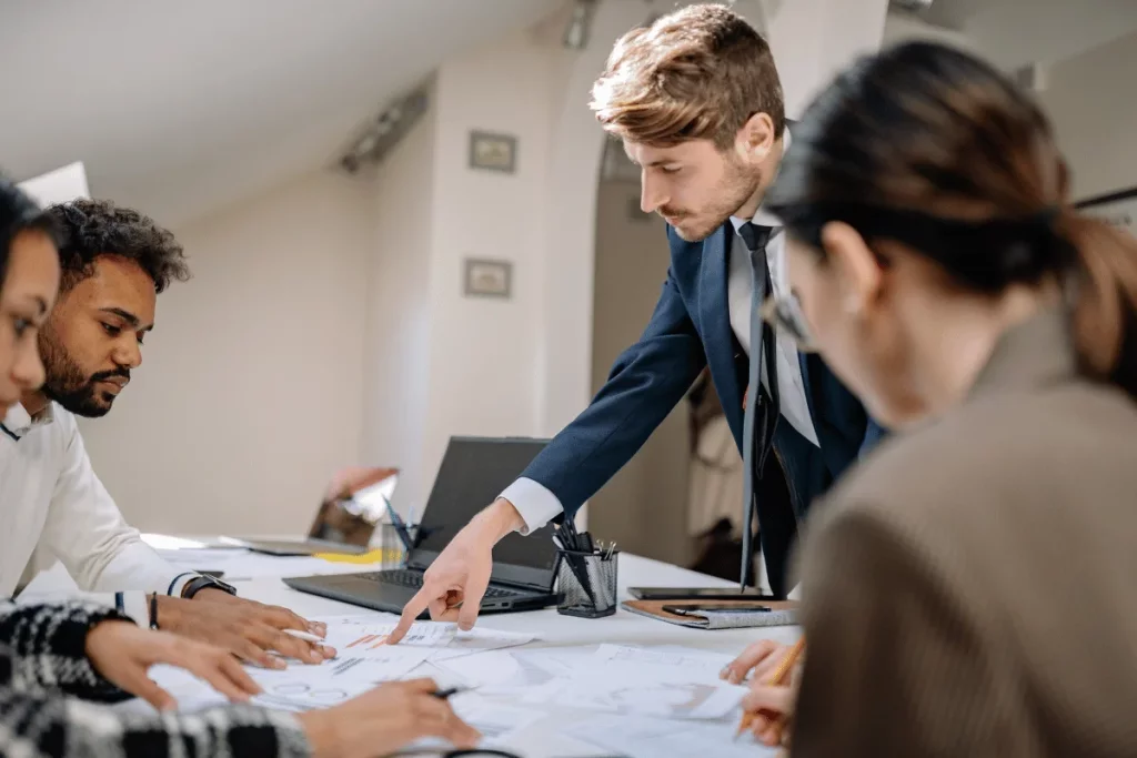 A professional workplace scenario with a team collaborating over financial reports and marketing charts on a large table.