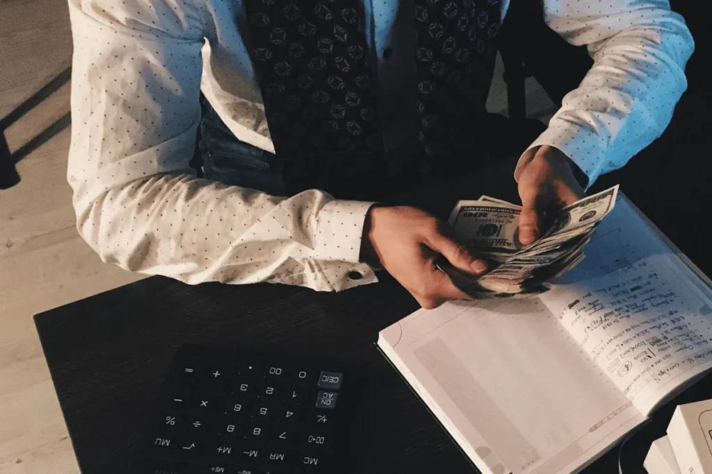 Close-up of a person handling cash while taking notes, with a calculator nearby.