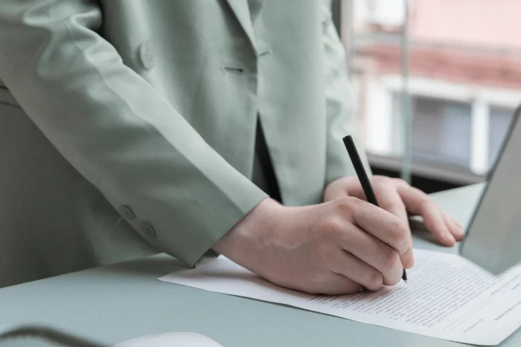 Person in a light green suit signing a document on a desk.