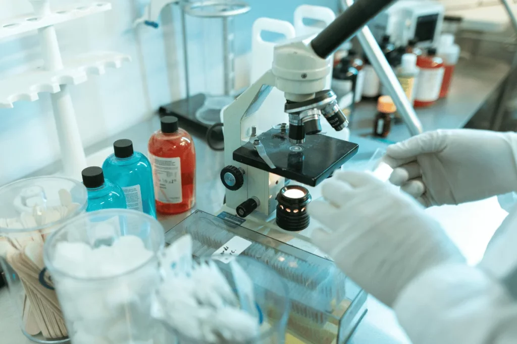 A scientist in white gloves prepares a microscope slide amidst colorful liquids and lab equipment on a clean laboratory workspace.