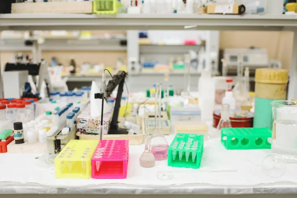A busy laboratory table cluttered with colorful test tubes, flasks, and various lab equipment, with a bright, organized workspace.