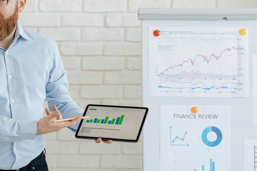 Business professional presenting financial data on a tablet with charts in background.
