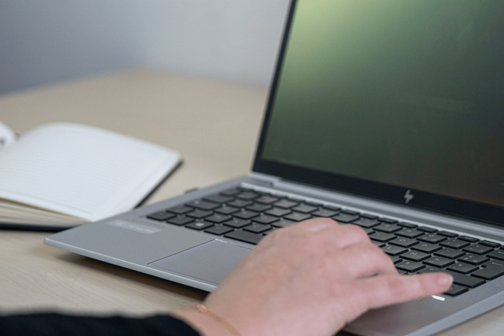 Person working on a laptop with a notebook and pen on the side.